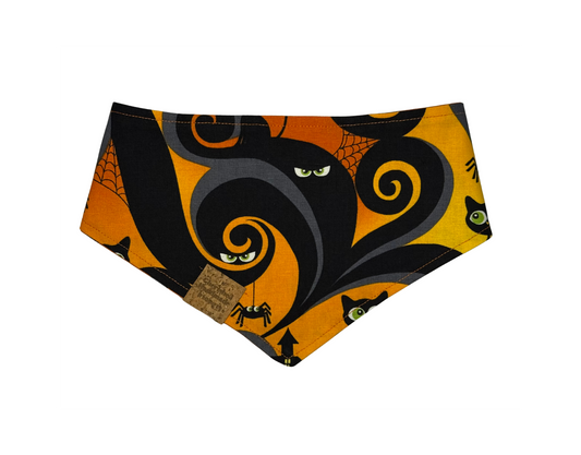 A triangular pet bandana featuring a Halloween-themed print with a large black cat silhouette, orange swirls, spiderwebs, spiderbugs, and cat faces on a bright orange background.